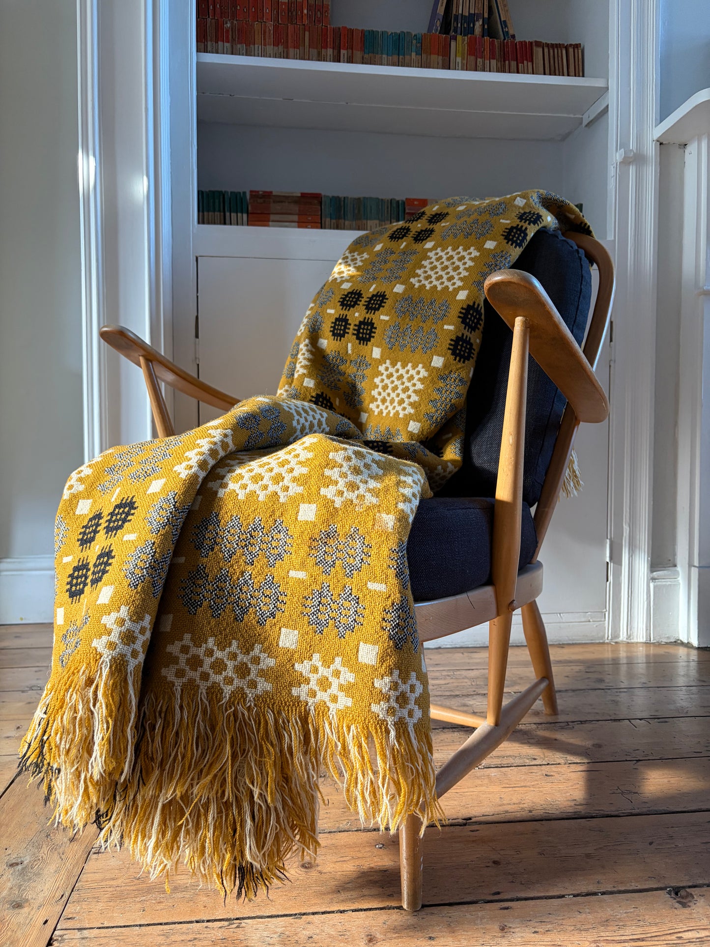 ELFYN Mustard yellow WELSH WOOL tapestry blanket  or throw draped over an Ercol chair in a room with wooden floors. Cymraeg Cymru